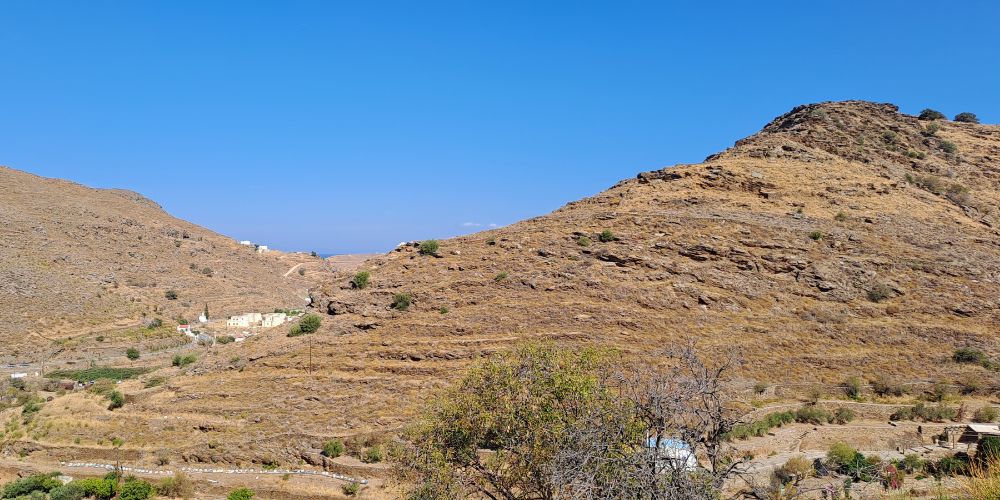 Dry, rocky mountain landscape with scattered buildings and clear blue sky in the background.