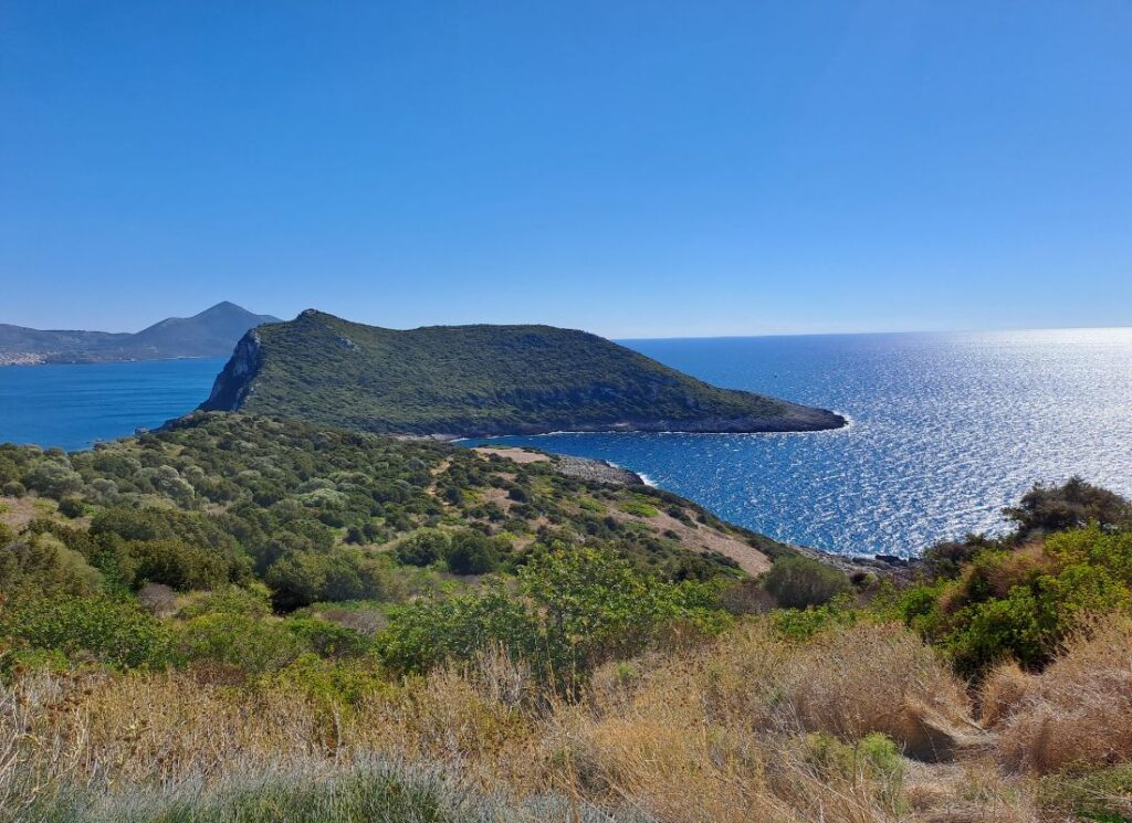 Coastal hiking view above Voidokilia Beach, showing a green peninsula and sparkling Ionian Sea near Pylos, Greece.