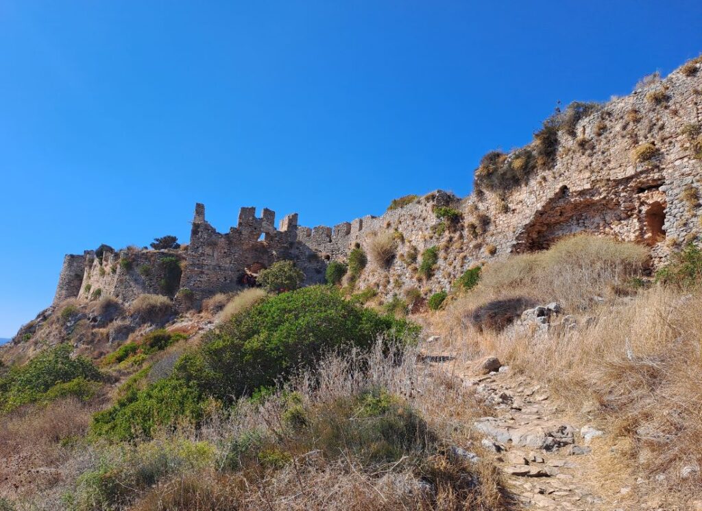 Hikers walking along the ancient walls of Paleokastro castle overlooking the Ionian Sea near Voidokilia Beach, Greece.