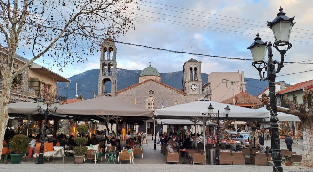 Vytina’s main square on Menalon Trail 5, with outdoor cafes, traditional buildings, and the church set against the mountains in Arcadia, Greece.