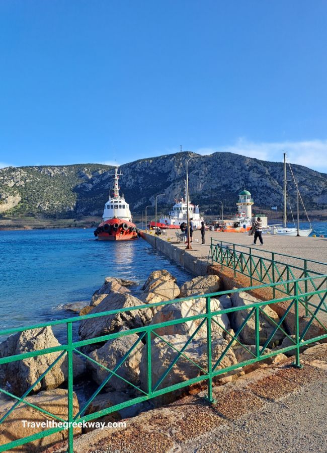 Tugboats docked at a pier with a lighthouse and mountains in the background.