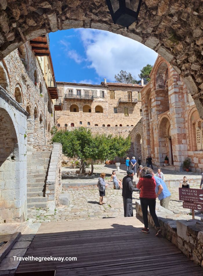 Visitors in the courtyard of a historic Byzantine monastery with stone archways and ancient buildings.