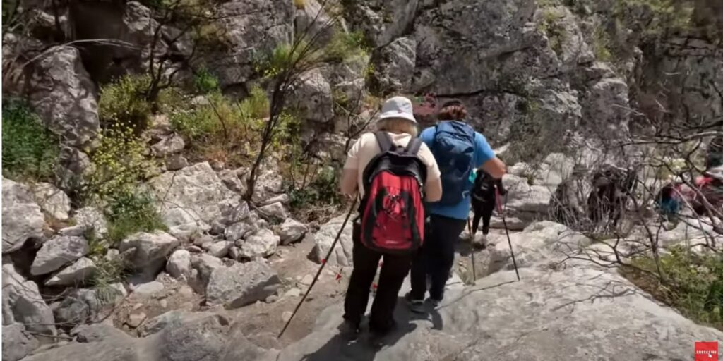 Hikers with backpacks and walking sticks navigating a rocky trail through a gorge.