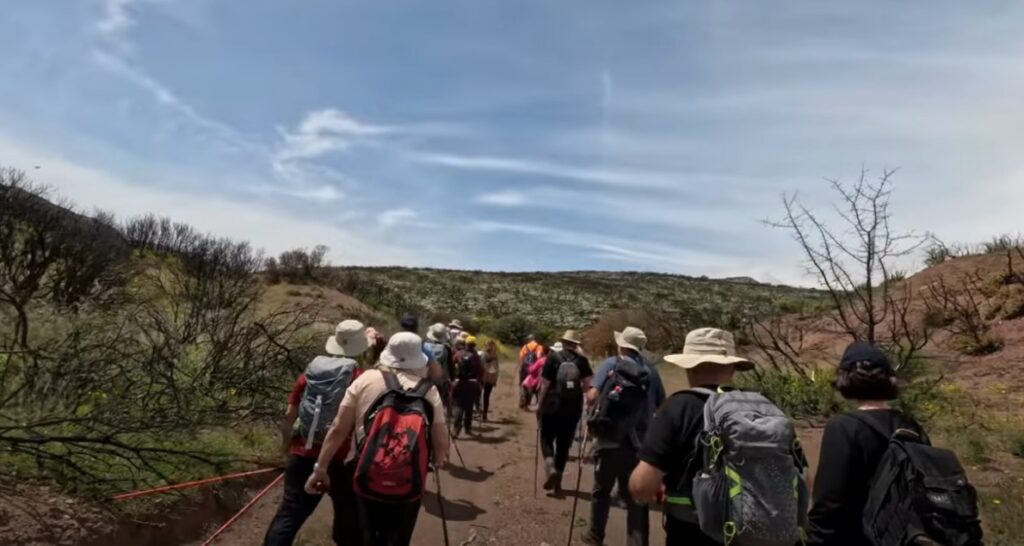 Group of hikers walking on a dirt road through a rugged landscape under a clear sky.