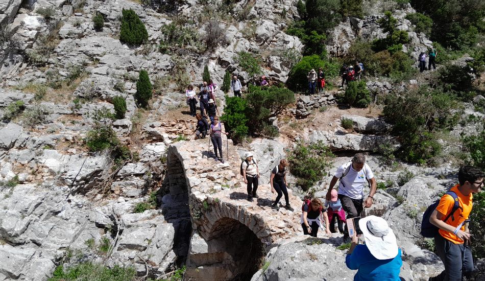 Group of hikers crossing a stone bridge in the rugged landscape of the Kleisoura Gorge.