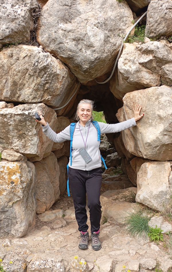 A woman smiling at the entrance of an Mycenaean Bridges in the Peloponnese framed by large weathered rocks.