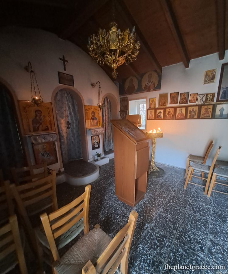 Small Greek chapel interior in Loutraki with wooden chairs, religious icons, candles, and a golden chandelier.