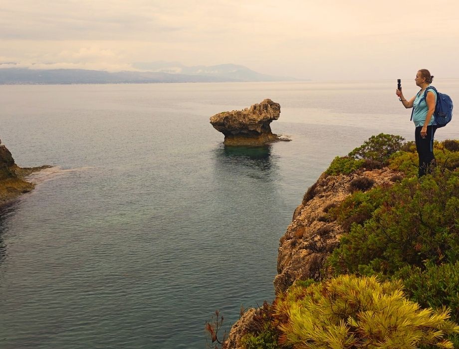 Evgenia filming sea view on the trail while hiking to Melagkavi Lighthouse in Loutraki Greece.