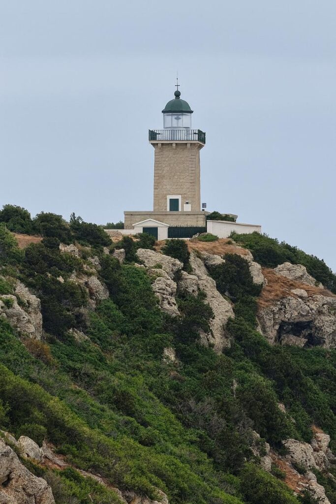 Melagkavi Lighthouse standing on rocky cliffs surrounded by greenery in Loutraki, Greece.