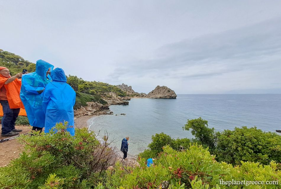 Hikers in colorful raincoats overlooking a small cove on the scenic hike to Melagkavi Lighthouse in Loutraki Greece.