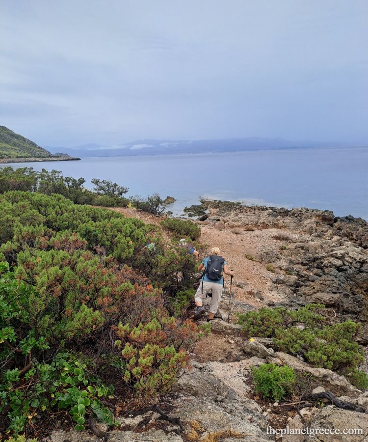 Hikers walking along the rocky coastline on the scenic Melagkavi Lighthouse hike in Loutraki Greece