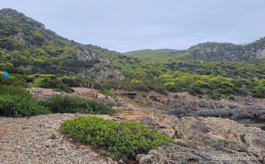Hikers passing through rocky terrain and wild herbs on the hike to Melagkavi Lighthouse in Loutraki Greece.
