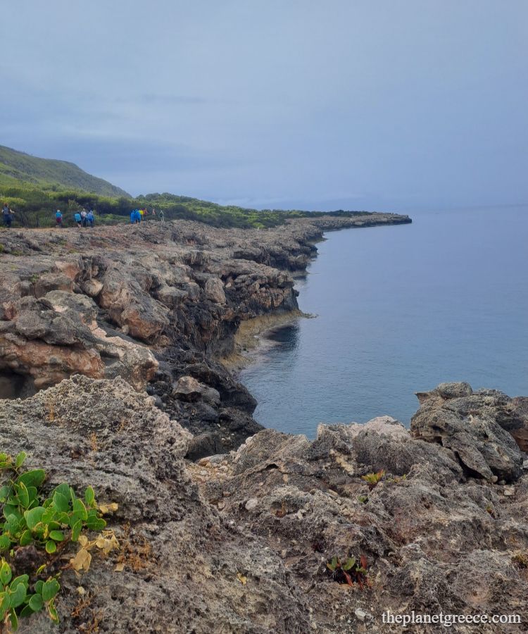 Rocky coastline and hikers enjoying the Melagkavi Lighthouse trail in Loutraki Greece.