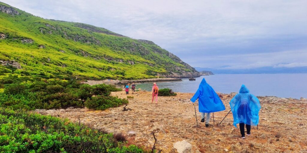 Hikers in blue raincoats walking the coastal trail to Melagkavi Lighthouse in Loutraki Greece.