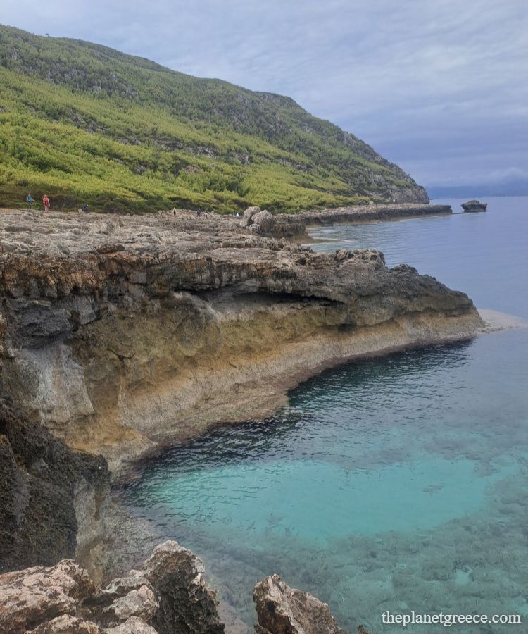 Hikers exploring rocky cliffs surrounded by green hills near Melagkavi Lighthouse in Loutraki Greece.