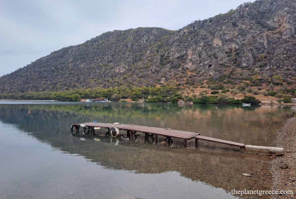 Wooden pier stretching into the calm waters of Vouliagmeni Lake, surrounded by rocky hills in Loutraki, Greece.